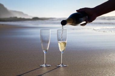 Gün batımında beyaz kumlu okyanus sahilinde Cava ya da şampanya dökmek.