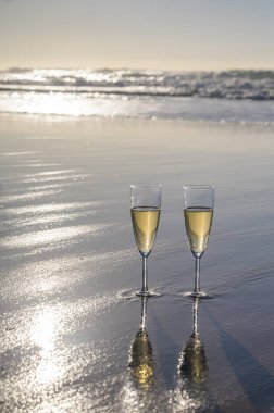 Kava bardakları ya da şampanya beyaz kumlu okyanus sahilinde köpüklü şarap. Gün batımında gölgeli güneş dalgaları.