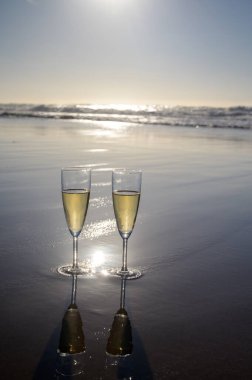 Kava bardakları ya da şampanya beyaz kumlu okyanus sahilinde köpüklü şarap. Gün batımında gölgeli güneş dalgaları.
