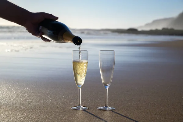 Pouring of cava or champagne sparkling white wine on white sandy ocean beach on sunset in sunlights