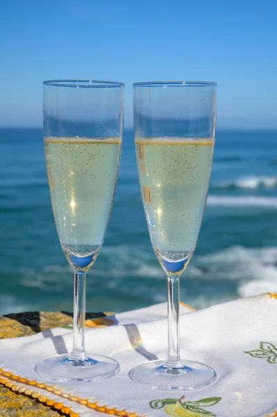 Glasses of champagne sparkling wine and sunny view on blue Atlantic ocean, Lisbon area, Portugal