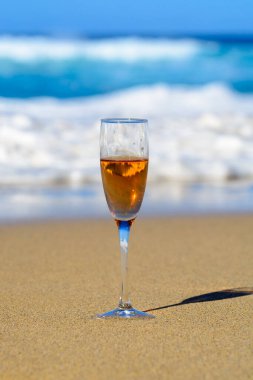 One glass of rose champagne or cava sparkling wine served on white sandy tropical beach and blue ocean water, romantic vacation, winter sun on Fuerteventura, Canary, Spain