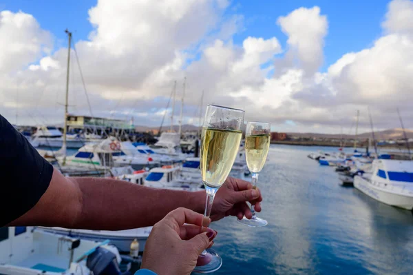 Everyday party, hands with glasses of cava or champagne sparkling wine in yacht harbour of Caleta de Fuste, Fuerteventura, Canary islands vacation, Spain