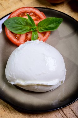 White ball of Italian soft cheese Mozzarella di Bufala Campana served with fresh green basil and red tomato, close up