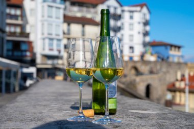 Tasting of txakoli or chacol slightly sparkling very dry white wine produced in Spanish Basque Country with view on port and sunny village Getaria, Spain