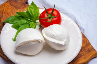 Beyaz İtalyan yumuşak peyniri Mozzarella di Bufala Campana topu taze yeşil fesleğen yaprakları ve kırmızı domatesle servis edilir.