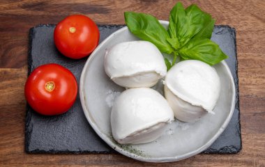 Beyaz İtalyan yumuşak peyniri Mozzarella di Bufala Campana topları taze yeşil fesleğen yaprakları ve kırmızı domatesle servis edilir.
