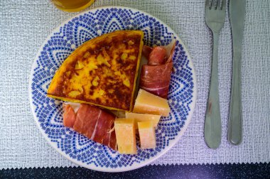 Spanish food, portion of potato omelette tortilla de patatas with onion served with cheese and jamon in cafe