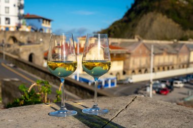 Tasting of txakoli or chacoli slightly sparkling very dry white wine produced in Spanish Basque Country with view on old port and sunny village Getaria, Spain
