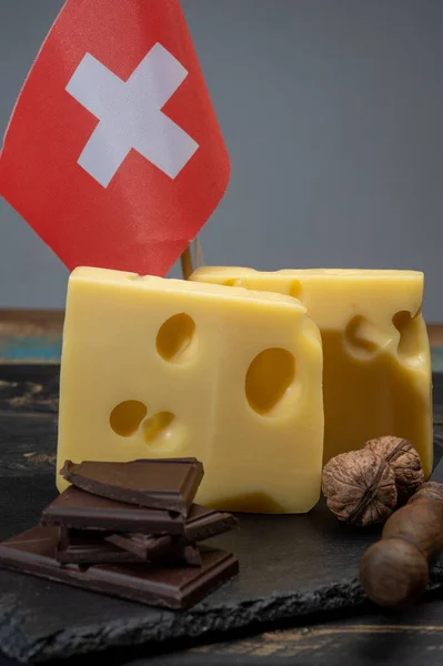 Swiss food, medium-hard cow milk cheese emmentaler with holes, dark swiss chocolate and flag of Switzerland close up