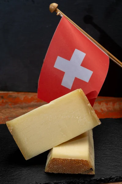 Swiss medium-hard cow milk cheese Gruyere, appenzeller used for traditional cheese fondue and gratin and flag of Switzerland on dark background