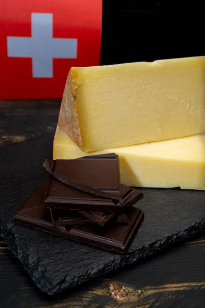 Swiss medium-hard cow milk cheese Gruyere, appenzeller, dark swiss chocolate and flag of Switzerland on dark background
