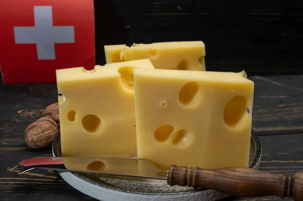 Block of Swiss medium-hard yellow cheese emmental or emmentaler with round holes and cheese knife and flag of Switzerland close up