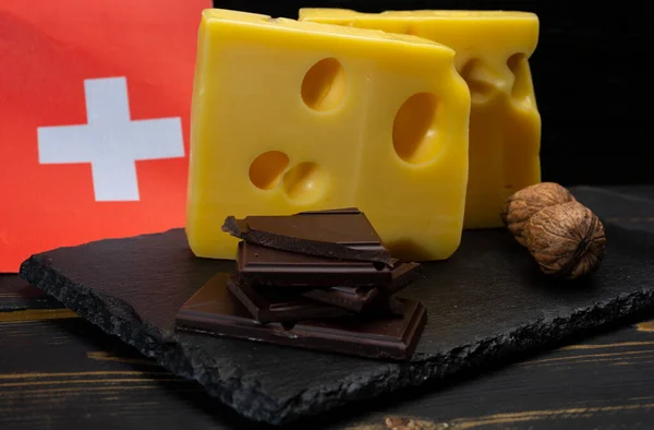 Swiss food, medium-hard cow milk cheese Gruyere, appenzeller, emmentaler with holes, dark swiss chocolate and flag of Switzerland on dark background