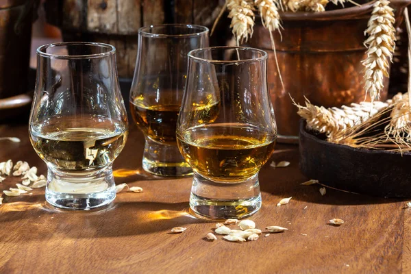 小さなテイスティングメガネで高齢者スコッチウイスキーで古いダークウッドのヴィンテージテーブルに大麦粒を閉じます — ストック写真