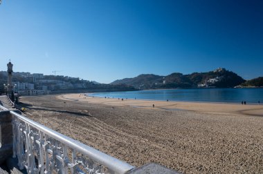 Walking on promenade along white sandy La Concha beach in central part of Donostia or San Sebastian city, Basque Country, Spain in sunny day