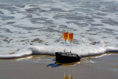 Two glasses of rose champagne or cava sparkling wine served on stone on white sandy tropical beach and blue ocean water, romantic vacation, winter sun on Fuerteventura, Canary, Spain