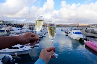 Everyday party, hands with glasses of cava or champagne sparkling wine in yacht harbour of Caleta de Fuste, Fuerteventura, Canary islands vacation, Spain