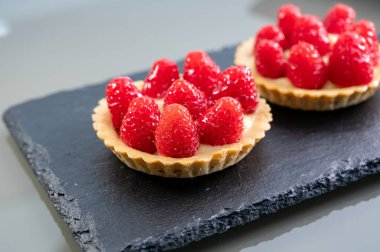 Artisanal baked small tart with cream and fresh ripe red raspberry, tasty french dessert