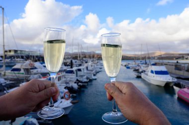 Everyday party, hands with glasses of cava or champagne sparkling wine in yacht harbour of Caleta de Fuste, Fuerteventura, Canary islands vacation, Spain