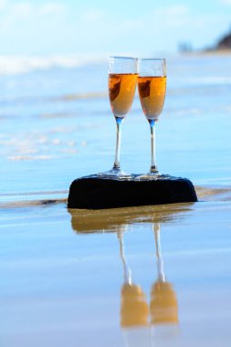 Two glasses of rose champagne or cava sparkling wine served on stone on white sandy tropical beach and blue ocean water, romantic vacation, winter sun on Fuerteventura, Canary, Spain