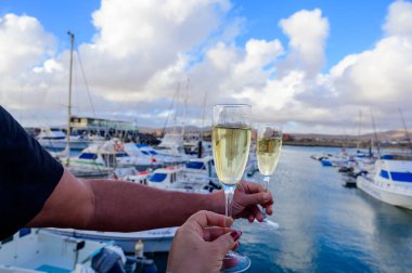 Everyday party, hands with glasses of cava or champagne sparkling wine in yacht harbour of Caleta de Fuste, Fuerteventura, Canary islands vacation, Spain