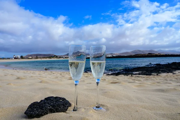 Stock image Two glasses of white champagne or cava sparkling wine served on white sandy tropical beach and blue ocean, romantic vacation, winter sun on Fuerteventura, Il Cotillo, Canary, Spain