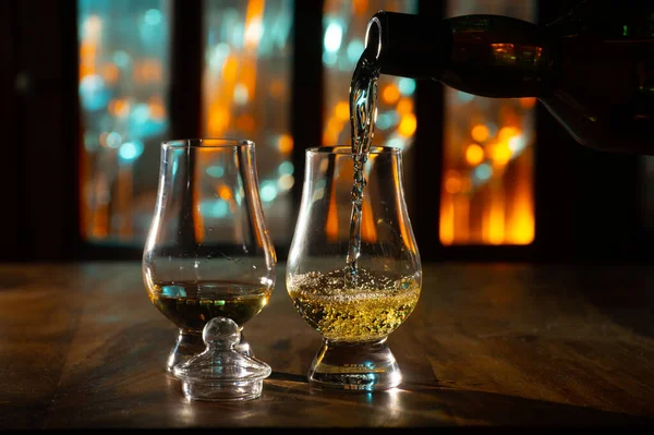 Pouring in tulip-shaped tasting glass Scotch single malt or blended whisky and whiskey bar on background