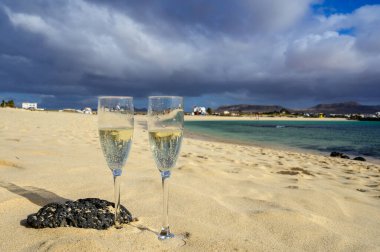 Two glasses of white champagne or cava sparkling wine served on white sandy tropical beach and blue ocean, romantic vacation, winter sun on Fuerteventura, Il Cotillo, Canary, Spain