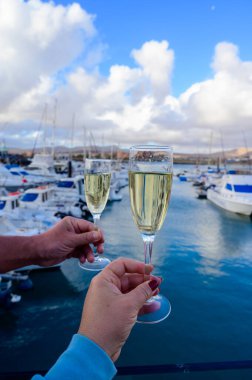 Everyday party, hands with glasses of cava or champagne sparkling wine in yacht harbour of Caleta de Fuste, Fuerteventura, Canary islands vacation, Spain