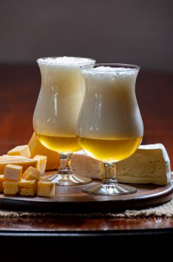 Manastırda yapılmış Belçika yapımı açık sarı bira bardakları ve çeşitli Belçika peynirleri, yiyecek ve bira eşleştirmeleri.