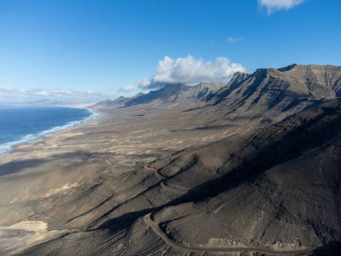 Fuerteventura, Kanarya Adaları, İspanya 'daki sıradağların arkasına gizlenmiş altın kumlu kahve plajına giden tehlikeli dar bir yol.