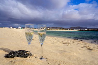 Two glasses of white champagne or cava sparkling wine served on white sandy tropical beach and blue ocean, romantic vacation, winter sun on Fuerteventura, Il Cotillo, Canary, Spain