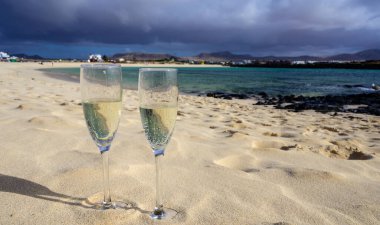 Two glasses of white champagne or cava sparkling wine served on white sandy tropical beach and blue ocean, romantic vacation, winter sun on Fuerteventura, Il Cotillo, Canary, Spain