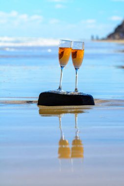 Two glasses of rose champagne or cava sparkling wine served on stone on white sandy tropical beach and blue ocean water, romantic vacation, winter sun on Fuerteventura, Canary, Spain