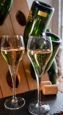 Glasses of sparkling white wine champagne gran cru or cava with bubbles and classic wooden champagne pupitre rack with empty bottles on background