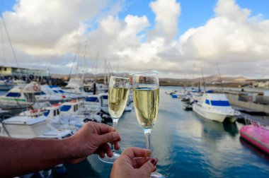 Everyday party, hands with glasses of cava or champagne sparkling wine in yacht harbour of Caleta de Fuste, Fuerteventura, Canary islands vacation, Spain