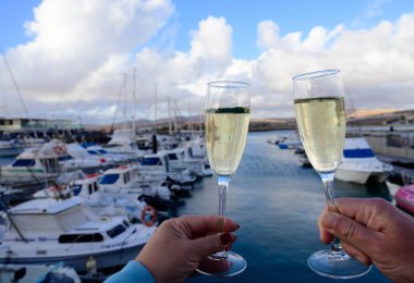 Everyday party, hands with glasses of cava or champagne sparkling wine in yacht harbour of Caleta de Fuste, Fuerteventura, Canary islands vacation, Spain