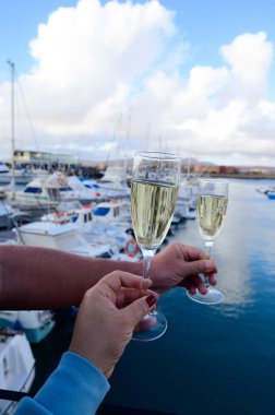 Everyday party, hands with glasses of cava or champagne sparkling wine in yacht harbour of Caleta de Fuste, Fuerteventura, Canary islands vacation, Spain