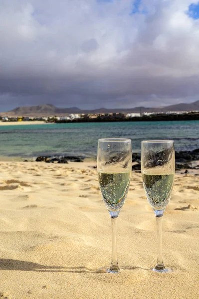 stock image Two glasses of white champagne or cava sparkling wine served on white sandy tropical beach and blue ocean, romantic vacation, winter sun on Fuerteventura, Il Cotillo, Canary, Spain