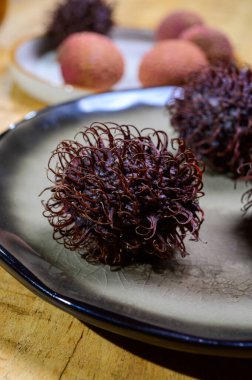 Tasty tropical exotic fruits, sweet ripe fresh unpeeled hairy rambutan southeast Asian fruits , close up