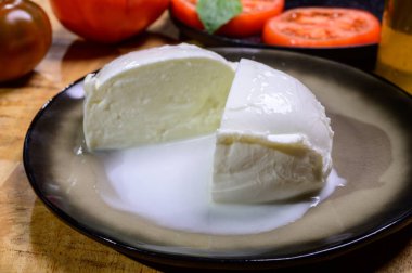 White ball of Italian soft cheese Mozzarella di Bufala Campana served with fresh green basil and red tomato, close up