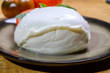 White ball of Italian soft cheese Mozzarella di Bufala Campana served with fresh green basil and red tomato, close up