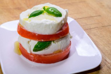 Sliced white ball of Italian soft cheese Mozzarella di Bufala Campana served with fresh green basil and red tomato, close up