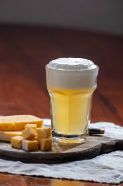 Bir bardak filtresiz Belçika birası kişniş ve turuncu akranlar ve inek sütünden yapılmış Belçika peyniri içeren ahşap pano.