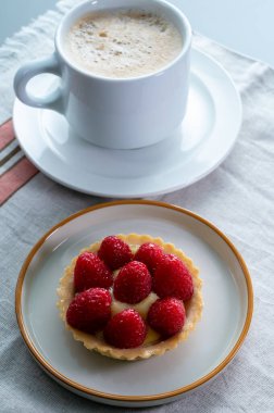 Breakfast with cup of black coffe and baked small tart with cream and fresh ripe red raspberry fruits close up