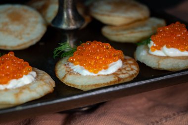 Tasty appetizer for dinner, small pancakes bliny with red fish caviar and sour cream close up