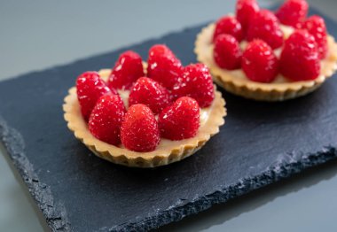 Artisanal baked small tart with cream and fresh ripe red raspberry, tasty french dessert