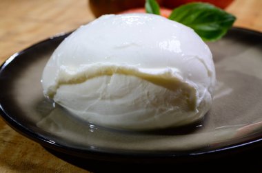 White ball of Italian soft cheese Mozzarella di Bufala Campana served with fresh green basil and red tomato, close up