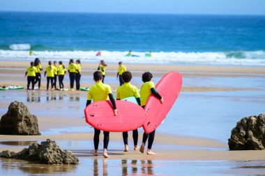 Genç sörfçüler, Celorio 'daki Playa de Palombina Las Camaras' ta, Kuzey İspanya, Asturias 'ın kumlu sahilleri, kayalıkları, gizli mağaraları, yeşil tarlaları ve dağları olan sörf tahtalimi yapıyorlar.